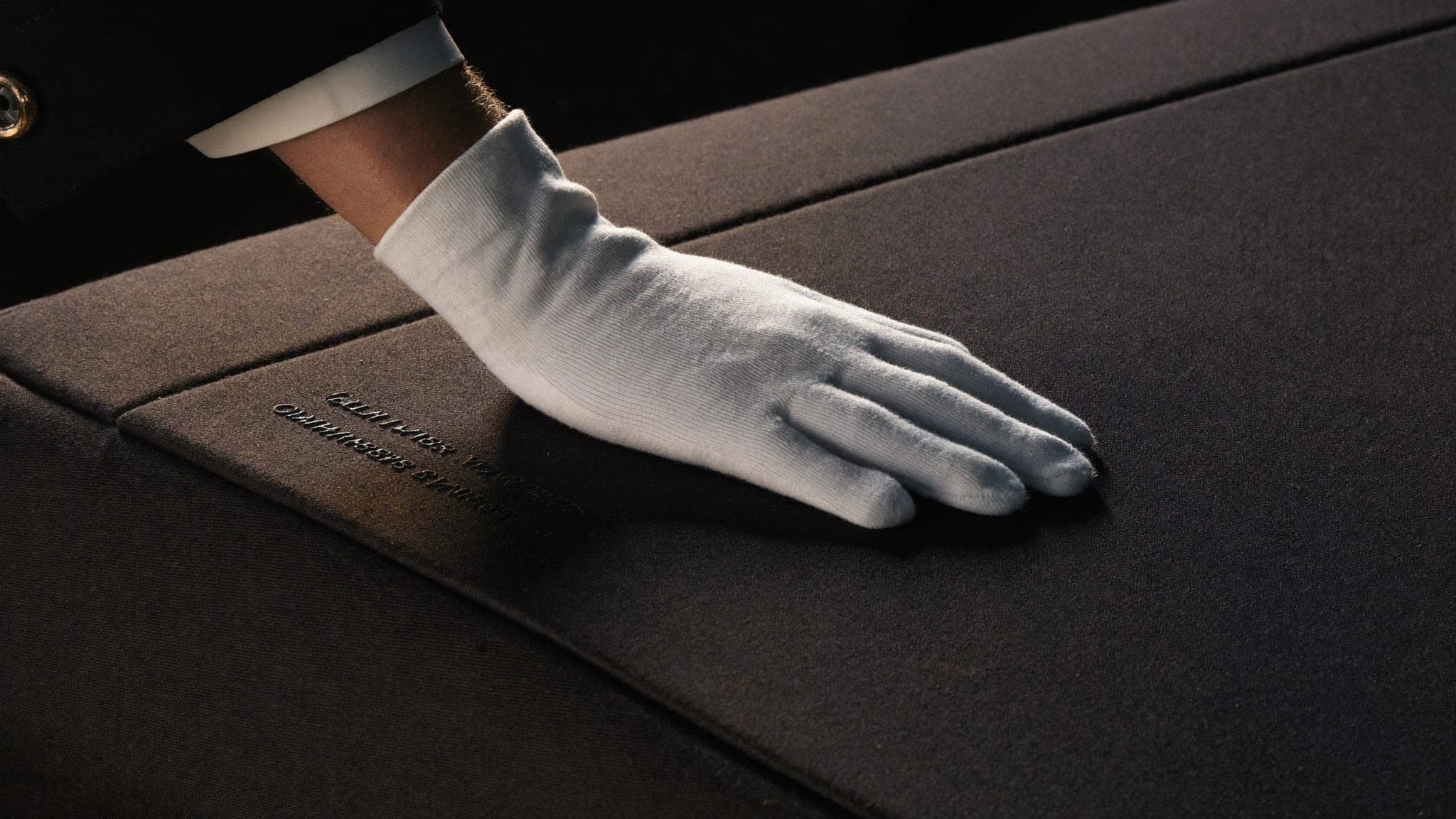 White-gloved hand resting on a tailored indoor car cover, a detail of Vault 620 concierge care